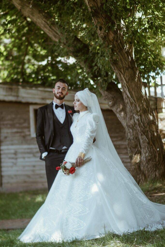 عروس وعريس في حديقة طبيعية مع شجرة كبيرة وخلفية خشبية.